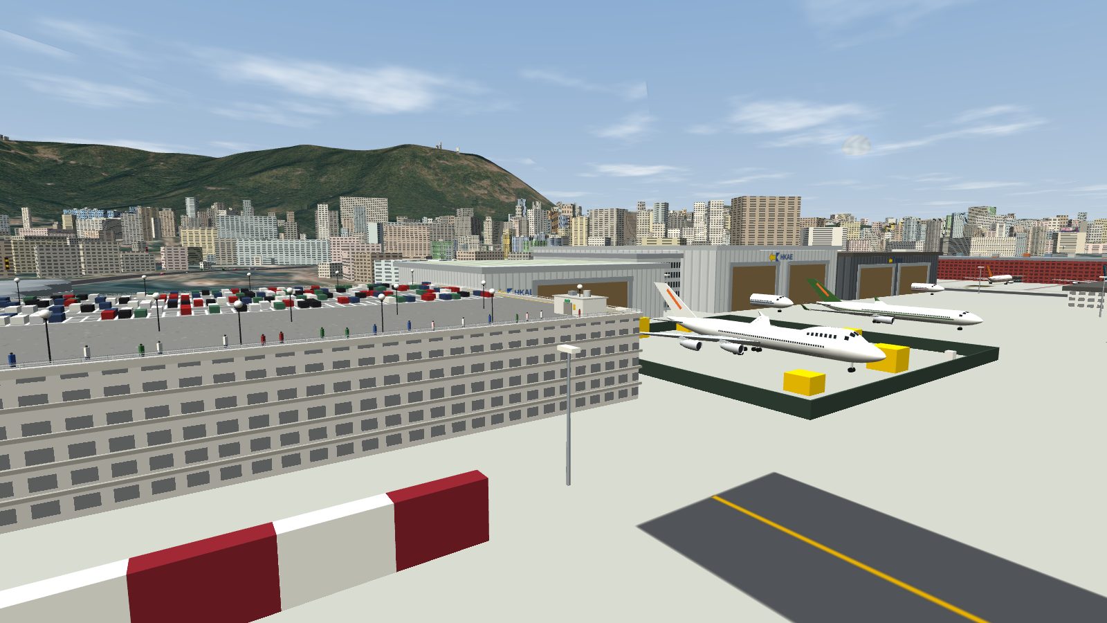 A stripped 747 inside a dark mesh fence with yellow stands, in front of the hangars, with the car park and striped blast fence in the foreground.